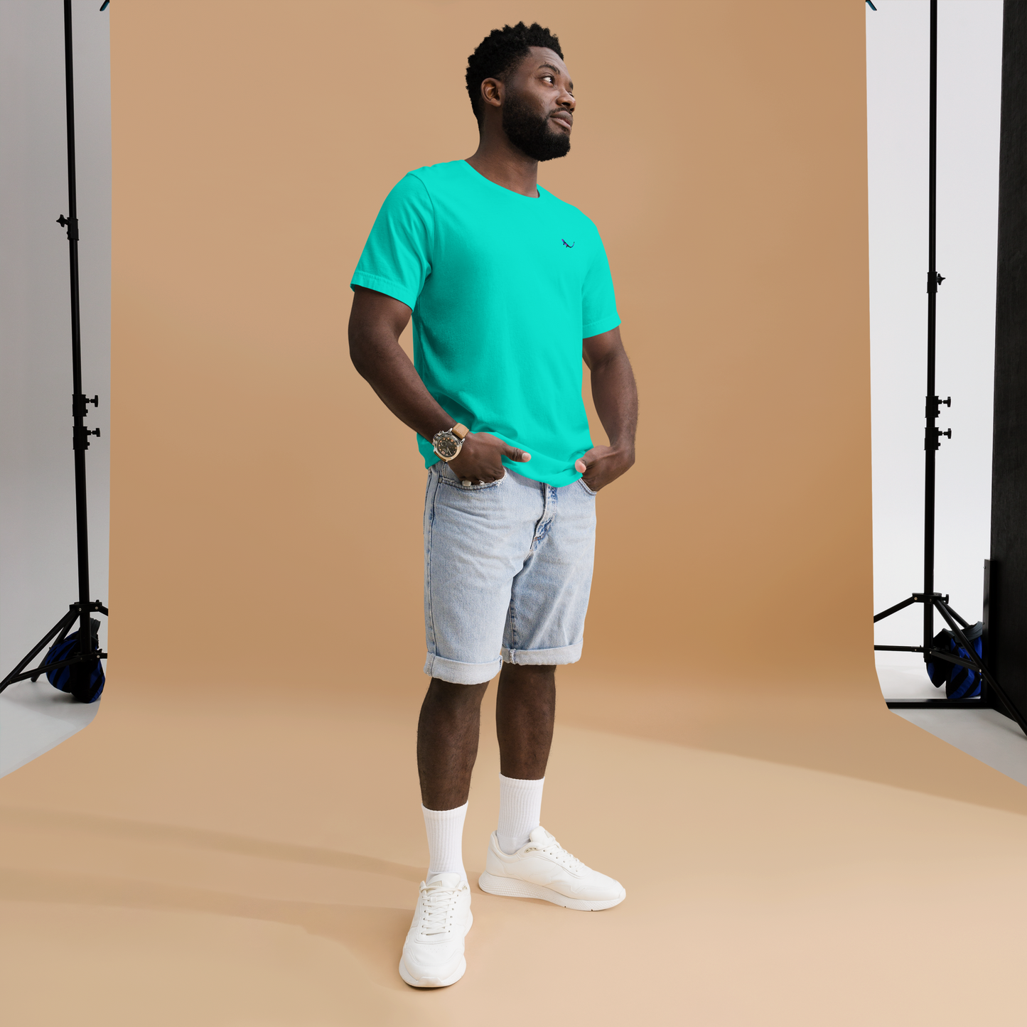 Model wearing THE SUBTROPIC Global Tee in teal with denim shorts against a neutral background.