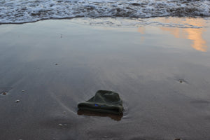 Black Organic Eco-Beanie sitting on sand with wave approaching
